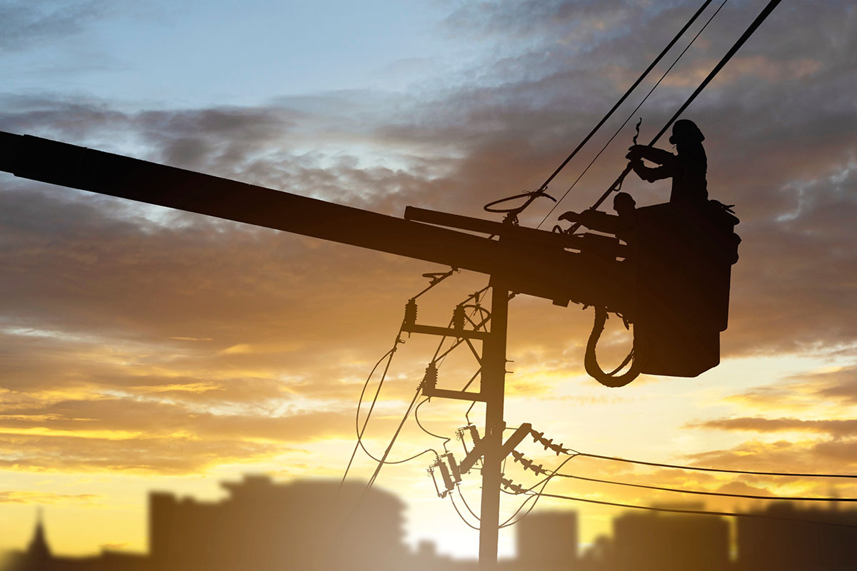 Maintenance of electricians working on high voltage on bucket silhouette on sunset background.