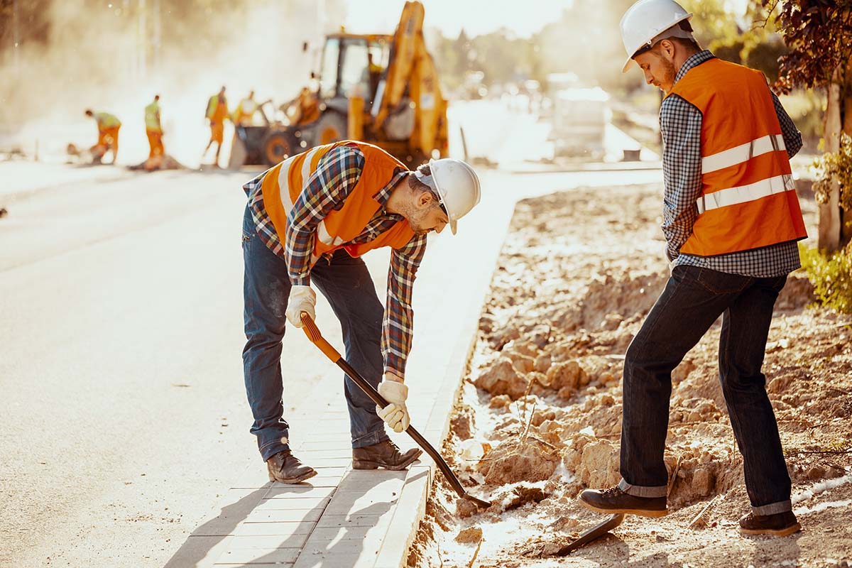 Workers in reflective vests using shovels during carriageway work.